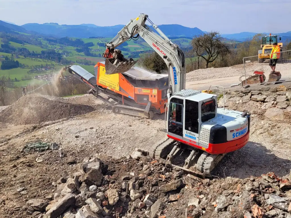 Bagger beim Verladen von Abbruchmaterial in eine mobile Brech- und Siebanlage.