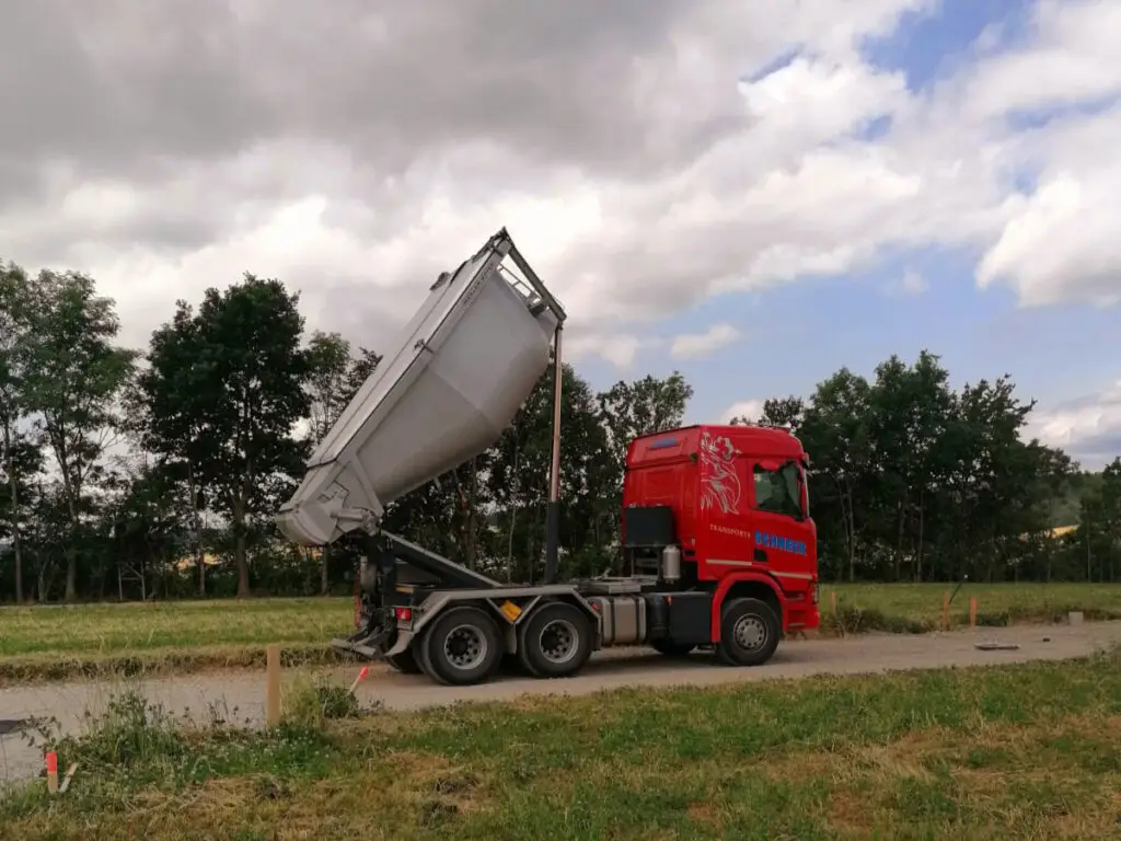 Scania-Asphaltmulde beim Entladen von Asphaltheißmischgut auf einer Straßenbaustelle.