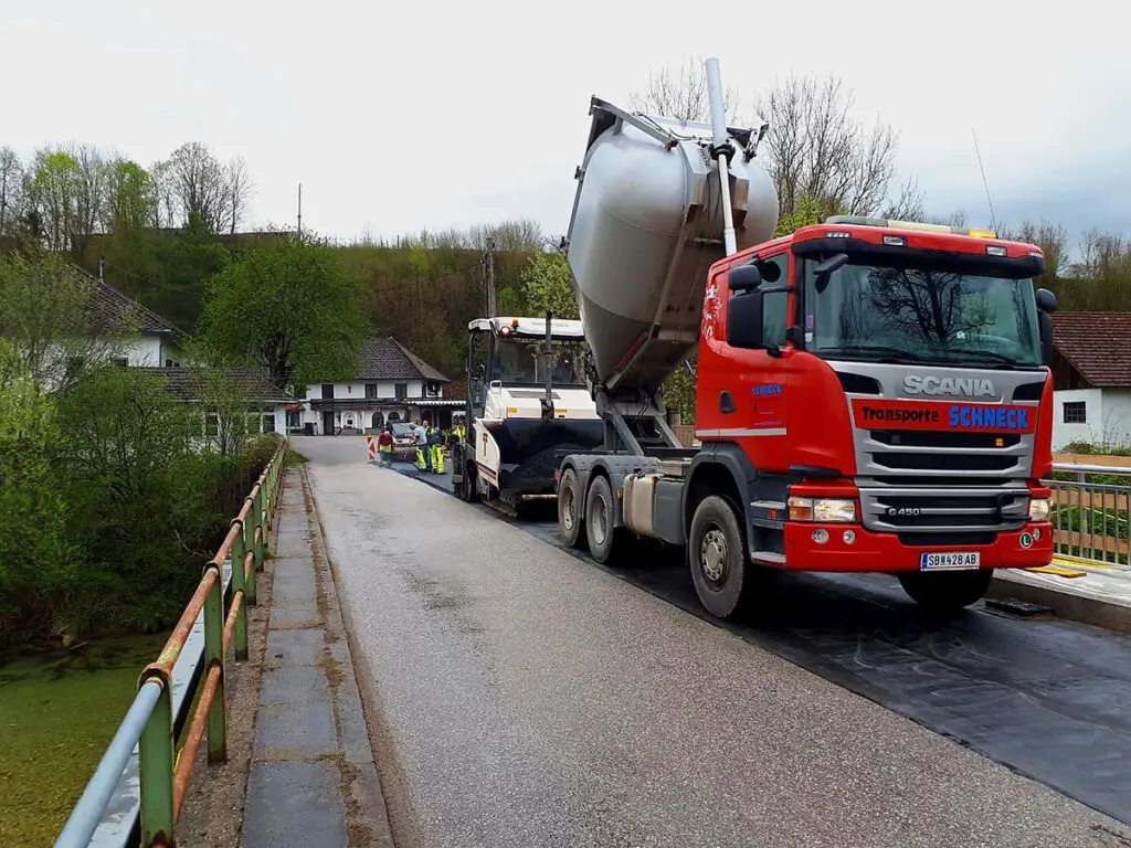 Asphalttransportfahrzeug auf einer Brücke während der Anlieferung von Asphalt für Straßenbauarbeiten.