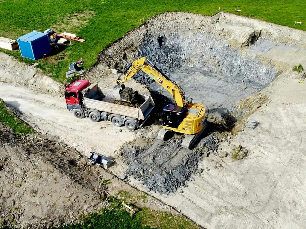 Aushub einer Baugrube mit Bagger und Muldenfahrzeug aus der Vogelperspektive.