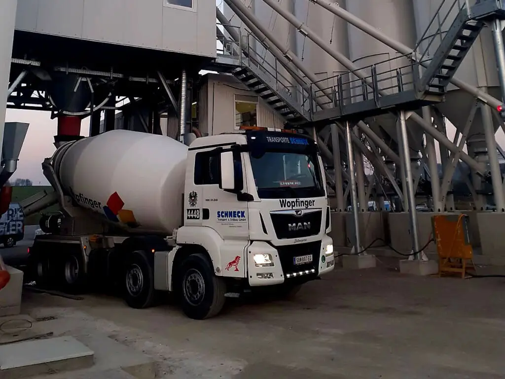 Betonmischer-LKW bei der Beladung in einem Betonwerk unter einer stationären Mischanlage.