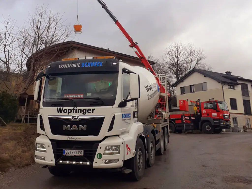 Betonmischer-LKW auf einer Baustelle mit Betonpumpe und weiterem Baustellenfahrzeug im Hintergrund.