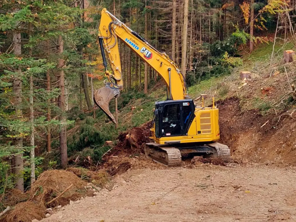 Bagger beim Ausbau einer Forststraße in steilem Waldgelände.
