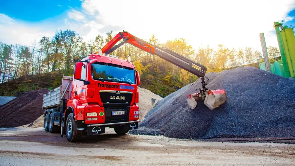 MAN-Kran-LKW von Schneck Transport & Erdbau beim Verladen von Schüttgut mit hydraulischem Greifer auf einem Lagerplatz für Baustoffe.