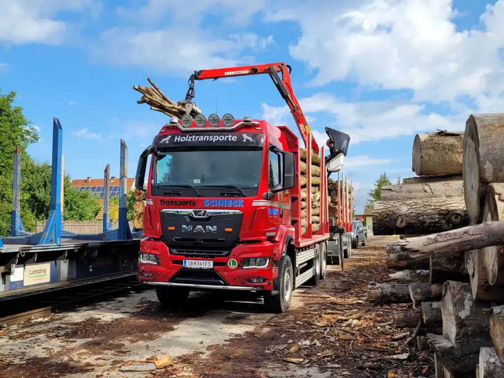 Holztransporter mit Ladekran beim Verladen von Rundholz am Holzlagerplatz.