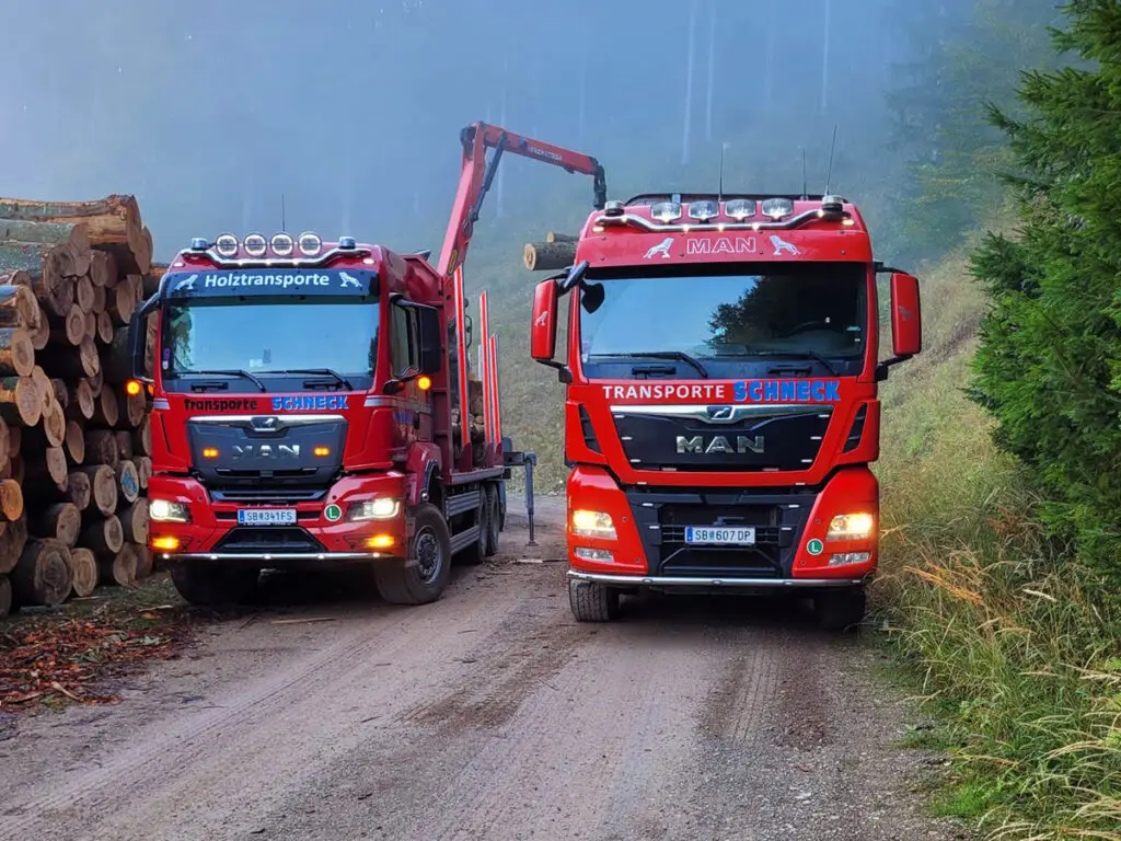 Zwei Schneck-Holztransporter bei der Rundholzverladung auf einer schmalen Forststraße.