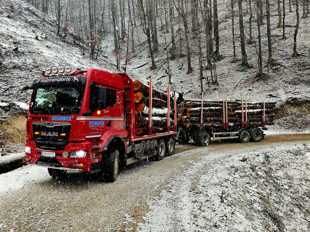Langholztransporter mit Rundholzladung auf verschneiter Forststraße im Wintereinsatz.