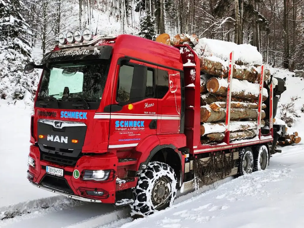 Beladener Schneck-Holz-LKW mit Schneeketten beim Rundholztransport im Winter.