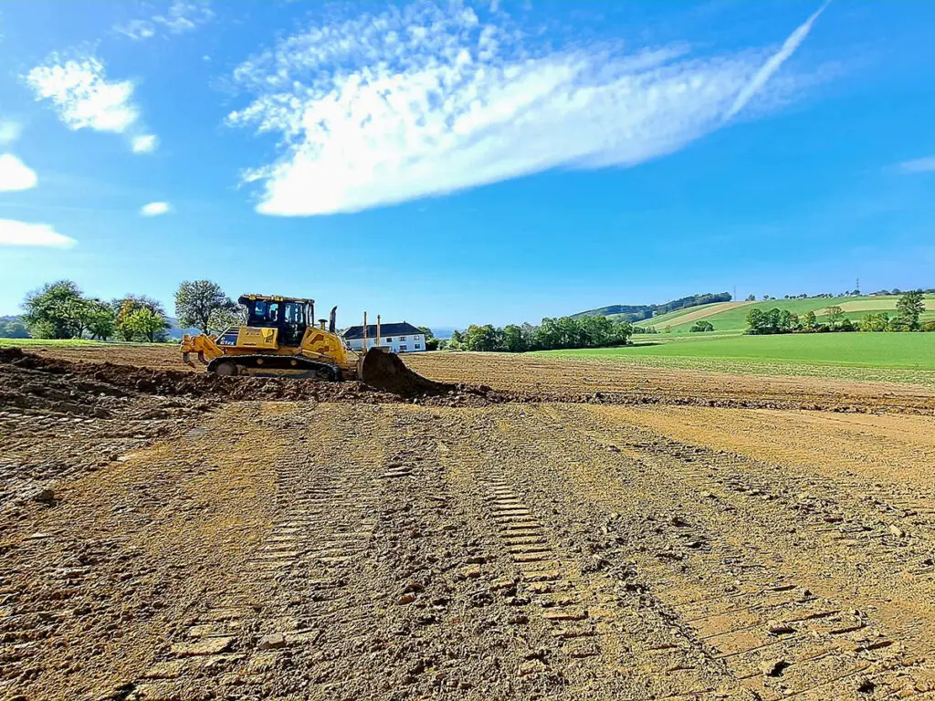 Motorgrader bei der präzisen Geländeplanierung einer großflächigen Erdbaustelle.