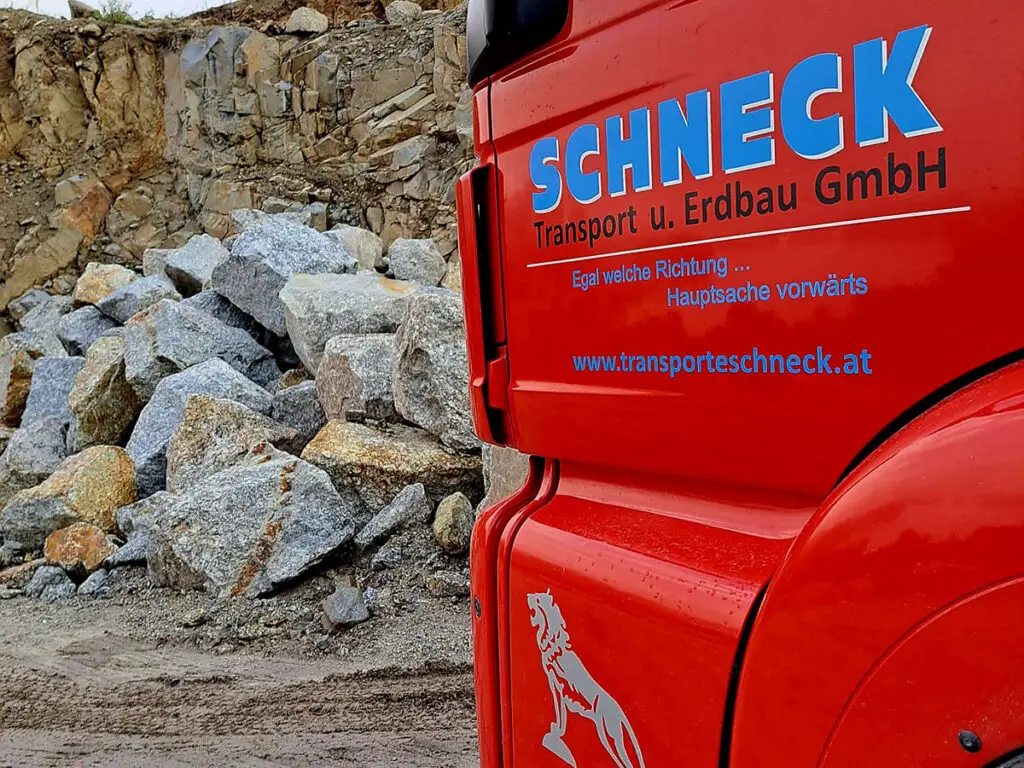 Schneck-LKW vor gelagerten Wasserbausteinen und Natursteinen für Erdbauprojekte.