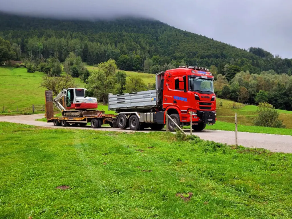 Tiefladertransport eines Baggers auf einer Landstraße im ländlichen Raum.