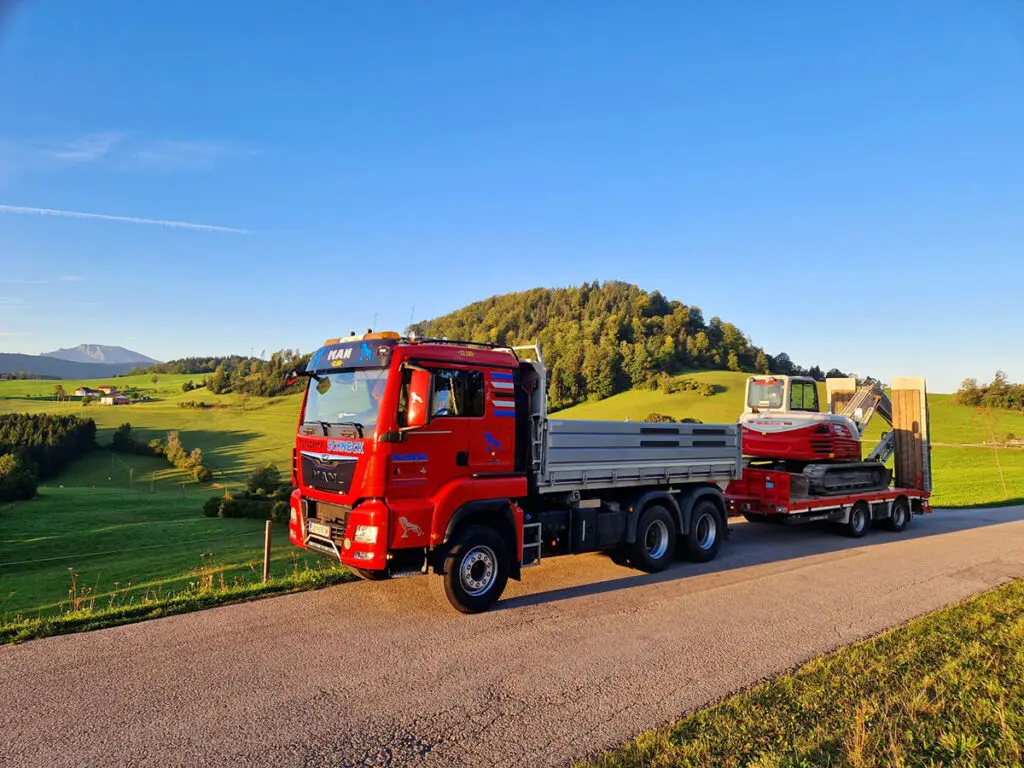 Tiefladertransport eines Baggers auf einer Landstraße im hügeligen Mostviertel.