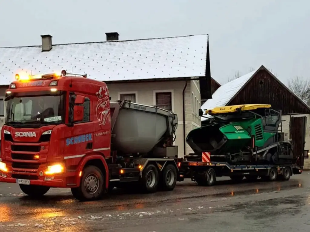 Sondertransport eines Straßenfertigers mit Tieflader auf einer Baustelle bei winterlichen Bedingungen.