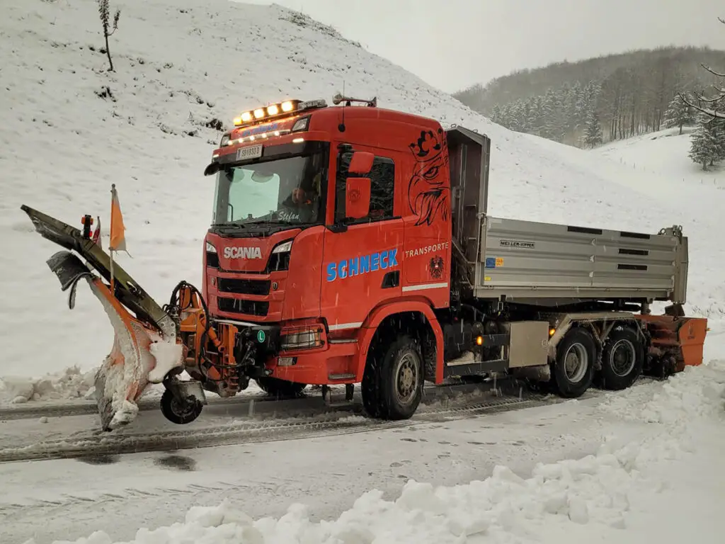 Winterlicher Sondertransport mit Schneepflug und Tieflader für Baumaschinen.