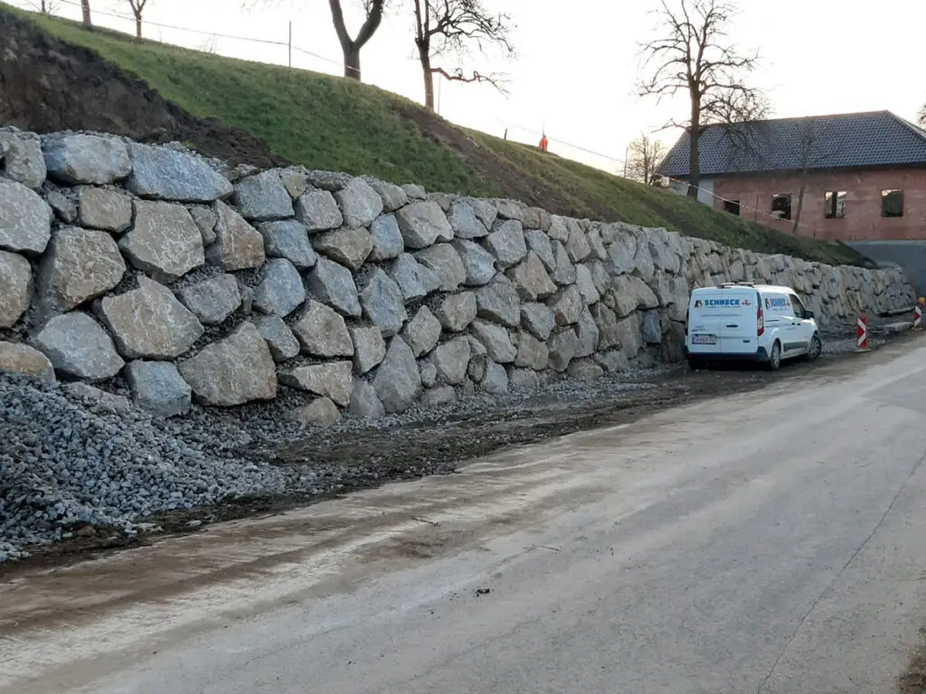 Lange Wurfsteinmauer entlang einer Straße zur dauerhaften Böschungs- und Hangsicherung.