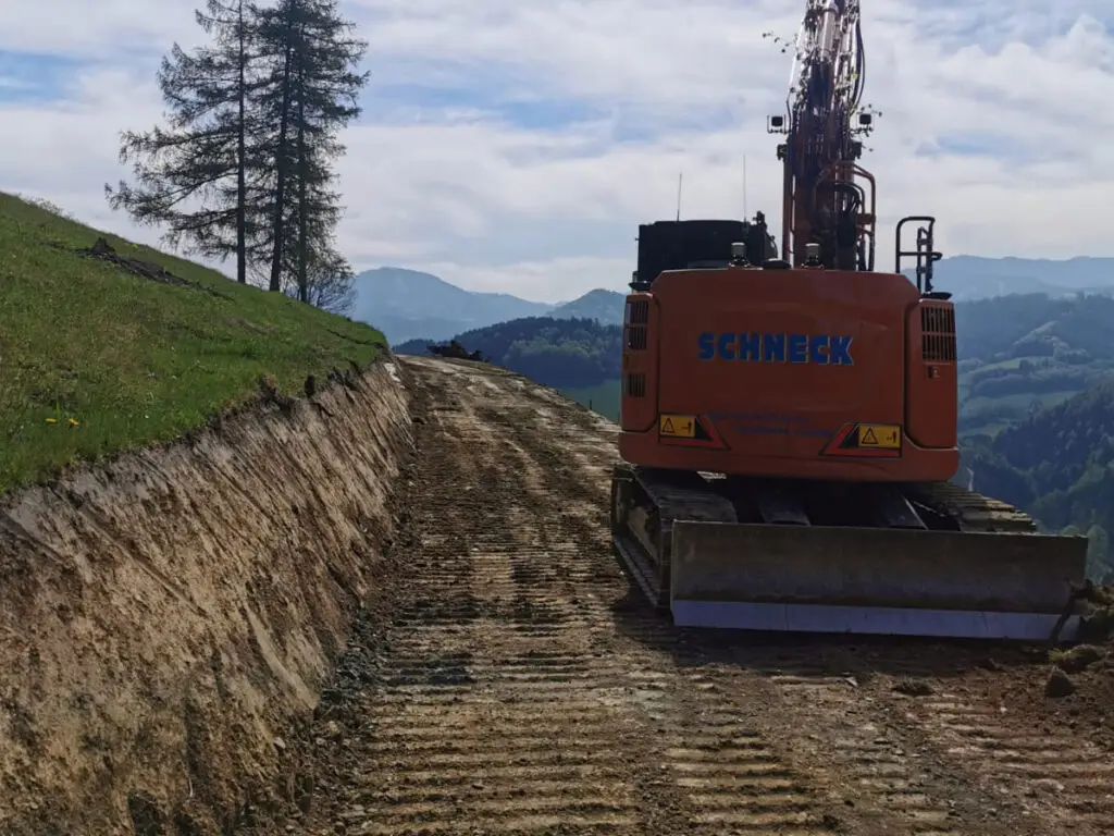 Herstellung eines Forst- und Güterweges mit Bagger entlang einer Böschung.